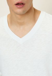 Baltos v-kaklo marškinėliai, pagaminti iš lengvo medvilnės. Pasižymi subtiliu tekstūriniu raštu ir lygiu kaklu, leidžiančiu laisvai jaustis.