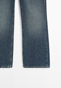 Proste nogawki niebieskich dżinsów z subtelnym spraniem i przeszytymi krawędziami na białym tle.