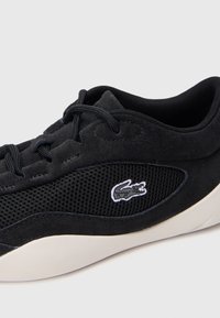 Zwarte sneaker met een combinatie van suède en mesh materialen, met een textuur en een wit geborduurd logo aan de zijkant.