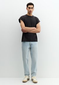 Schwarzes overSize T-Shirt mit umgeschlagenen Ärmeln, kombiniert mit hellblauen, ausgebleichten Jeans und beigen Sneakers mit dunklen Akzenten. Minimalistisches Design.