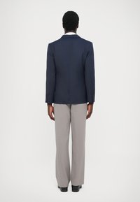 Tengerészkék blézer két gombbal, világosszürke nadrággal párosítva. Simaságot biztosító anyag, testhezálló fazonnal, amely tiszta vonalakat és strukturált designt mutat.