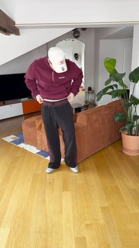 Bordeauxrode pullover met een ritssluiting tot een kwart, en zwarte joggingbroek met een elastische tailleband, staand op een houten vloer in een woonkamer.