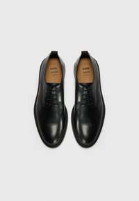 Black leather dress shoes with a smooth finish, six eyelets for laces, and a natural leather insole. Minimalist design with a rounded toe.