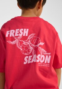 Röd bomullst-shirt med ett grafiskt tryck av fotbollar och löv, med texten "FRESH SEASON" i fet vit stil på baksidan.