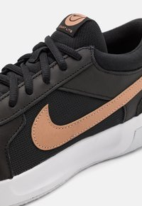 Sneaker nera realizzata in materiali mesh e sintetici, con un logo in pelle color cuoio, suola bianca e lacci neri. Accentuata da un'etichetta con il logo.