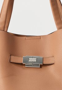 Sac à main en cuir fauve à surface texturée, doté d'un fermoir en métal argenté et d'un accent cousu. Deux poignées robustes sont visibles.