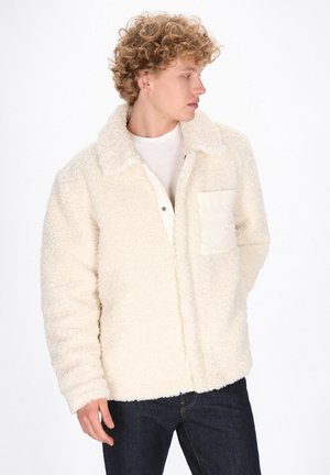 Fleece jacket in cream, featuring a collared design, button closure, and a chest pocket with a smooth, light-colored fabric accent.
