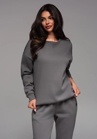 Sudadera gris de manga larga, con cuello redondo y puños de canalé, combinada con pantalones a juego. Material suave y texturizado. Acentos de logo.