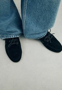 Zwarte suède schoenen met veters, gecombineerd met losse lichtblauwe denimbroek met een ontspannen pasvorm en rafelige zomen.