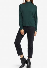 Maglione a collo alto verde scuro a maniche lunghe abbinato a jeans neri a vita alta e stivaletti neri alla caviglia. Tessuto liscio con una vestibilità comoda.