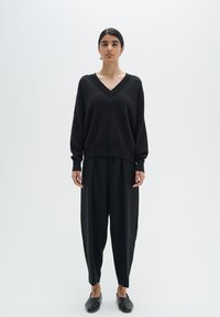 Black oversized sweater with a V-neck and long sleeves, paired with flowy black trousers, both featuring a smooth texture. Simple design.