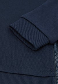 Navy blue zippered sweatshirt featuring ribbed cuffs and hem, made from a soft fabric with a smooth texture and subtle stitching details.