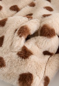 Couverture en fausse fourrure crème avec de grandes taches brunes irrégulières. Texture douce, design moelleux et tombé confortable. Convient pour une literie chaude.