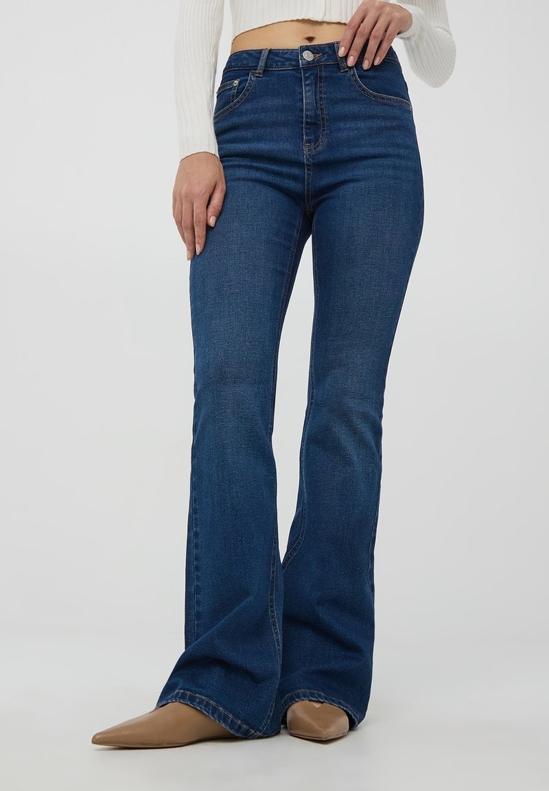 Jeans a vita alta svasati in denim blu scuro con cuciture sottili e tasche. Texture liscia e dritta con una larga svasatura all'orlo.