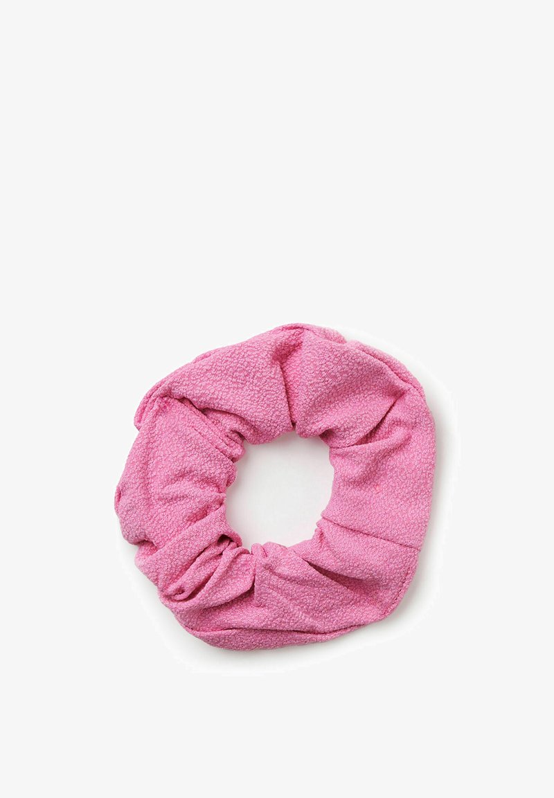 Chouchou en tissu rose avec une surface texturée, posé à plat en forme circulaire sur un fond blanc.