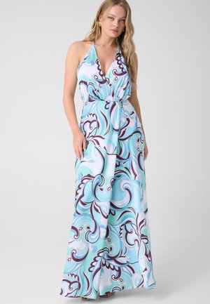 Frau trägt ein ärmelloses Maxikleid mit Neckholder und einem blau-weiß-lila wirbelnden Muster, stehend vor einem einfarbigen Hintergrund.