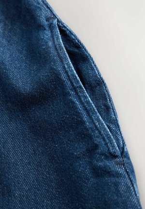 Tmavomodrá rifľovina s hladkou textúrou, zobrazujúca detailný záber švu a oblasti vrecka, zdôrazňujúci detaily šitia.