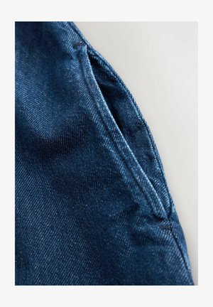 Tmavomodrá rifľovina s hladkou textúrou, zobrazujúca detailný záber švu a oblasti vrecka, zdôrazňujúci detaily šitia.