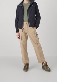 Navy windbreaker, olive green T-shirt, beige cargo pants with front pockets, and green hiking boots with brown laces. Casual outdoor outfit.