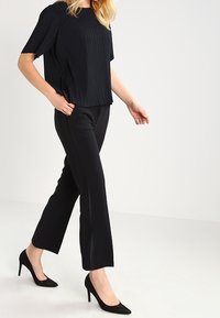 Svart, ribbad kortärmad topp kombinerad med åtsittande svarta byxor och spetsiga svarta klackskor. Byxorna har sidofransdetaljer.