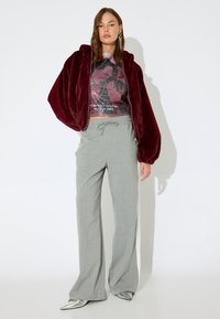 Bordeaux pluche ritsjack over een grafisch gebreid shirt, gecombineerd met lichtgrijze gestreepte wijde broek en metallic zilveren schoenen.
