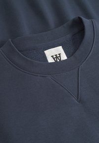 Dark navy sweatshirt with a crew neckline, ribbed cuffs, and a textured interior. Features a white tag with a logo inside the collar.