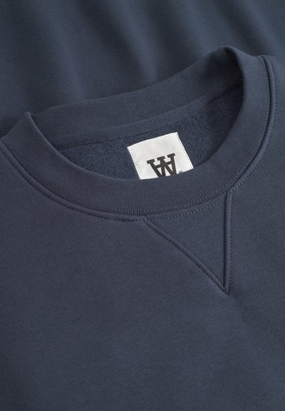Sweatshirt bleu marine foncé avec un col rond, des poignets côtelés et un intérieur texturé. Comprend une étiquette blanche avec un logo à l'intérieur du col.