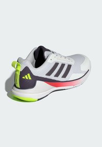 Chaussure de sport blanche avec un dessus texturé, accents violets, bande rose et détails réfléchissants jaunes sur le talon et les lacets.