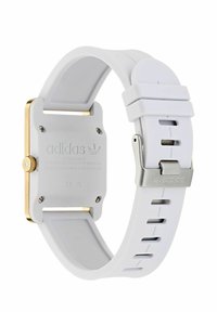 Montre avec bracelet en silicone blanc et un boîtier carré en ton doré, dotée d'un dos texturé et d'une boucle en acier inoxydable avec un logo gravé.