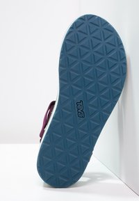 Suola di sandalo Teva con motivo geometrico blu e bordi della cinghia viola visibili su sfondo bianco.