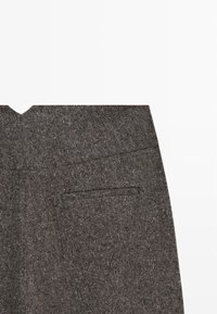 Tessuto struttura grigio scuro con un primo piano di una vita di pantaloni su misura e una tasca a filetto sul retro su uno sfondo bianco.