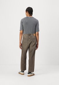 Gray short-sleeve t-shirt paired with loose-fit brown jeans. The jeans feature a leather patch and two back pockets. Footwear includes black and white sneakers.