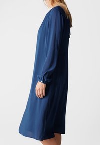 Abito lungo blu con maniche lunghe e vestibilità ampia, realizzato in tessuto leggero. Presenta bottoni ai polsini e un collo arrotondato.