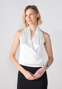 Vit halterneck-top i slätt satinmaterial, med en draperad design och en kortad nederkant. Bärs tillsammans med en svart kjol.