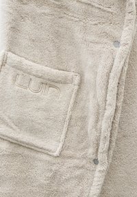 Beige, mjuk frottébadrock med en broderad ficka med "LUIN"-logotyp och en strukturerad yta med sydda kanter.
