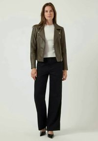 Oliven skinnjakke med sølvdetaljer, kombinert med en hvit tettsittende genser og høytlivte, svarte vide bukser.