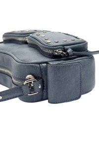 Niebieska skórzana torba o zaokrąglonym kształcie, z ozdobami w postaci srebrnych i złotych ćwieków na górze, podwójnymi zamkami błyskawicznymi oraz odpinanym paskiem po stronie.