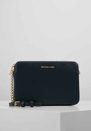 Zwart Michael Kors leren polstasje met gouden kettingriem en ritssluiting op een wit tentoonstellingsoppervlak.