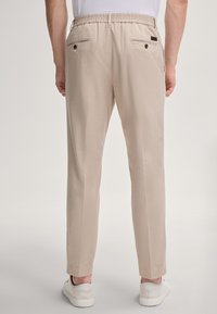 Pantaloni beige su misura con una cintura elastica, due tasche posteriori con bottone e una texture di tessuto leggera e liscia.