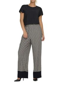 Un haut noir court associé à un pantalon large à motifs en design géométrique noir et blanc, comportant un ourlet bleu marine uni et des chaussures noires.