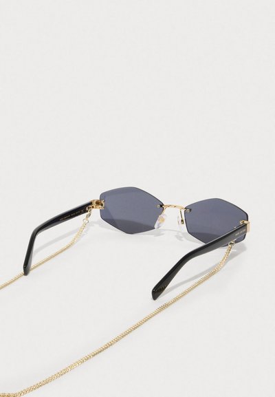 Εξάγωνα γυαλιά ηλίου με σκούρους φακούς και χρυσές μεταλλικές λεπτομέρειες; διαθέτουν μαύρους πλαστικούς βραχίονες και χρυσή αλυσίδα για ευκολία στη χρήση.