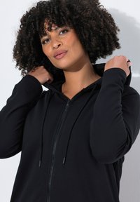 Sudadera con cremallera negra de textura suave, con cordones ajustables y un ajuste relajado. Incluye capucha forrada y cierre frontal con cremallera.