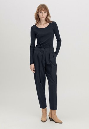Donkere lang-sleeve shirt met een scoop halslijn, gecombineerd met hoge taille, geplooide donkere broek en beige, met hakken, enkellaarsjes.
