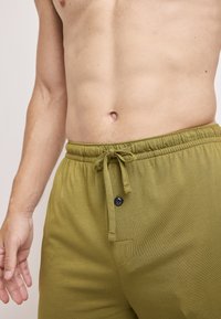Olive green cotton shorts with an elastic waistband, adjustable drawstring, and a decorative button on the front pocket.