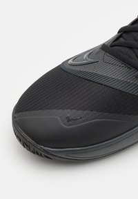 Pointe d'une chaussure de sport noire avec dessus en tissu texturé, semelle en caoutchouc et deux logos Nike swoosh, un grand près des lacets et un petit sur le côté.