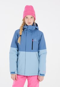 Giacca da sci blu e azzurro con colletto alto, tasca nera con zip e dettagli rosa, abbinata a un cappello lavorato a maglia rosa.