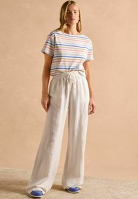 Striped cotton t-shirt in pastel colors paired with loose, white linen pants. The outfit features a relaxed fit and elastic waistband.