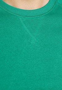 Sudadera de algodón verde con cuello redondo acanalado, costuras planas y textura suave. Presenta un brillo sutil y color sólido.