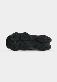 Semelle noire de chaussure de sport avec des motifs de bande de roulement en forme de diamant et le logo "new balance" au centre de la semelle.