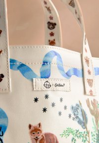 Płócienna torba na ramię z jasnym tłem, kolorowymi ilustracjami zwierząt, niebieskim wzorem fal oraz naszywką z logo. Wzmocnione uchwyty.